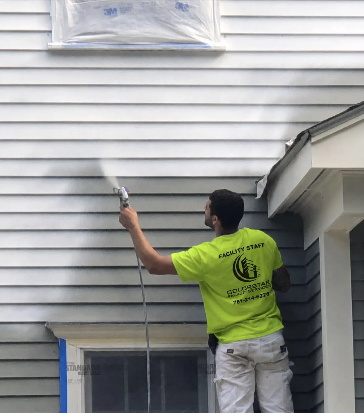 A Colorstar painter spray-painting the exterior siding of a New England home
